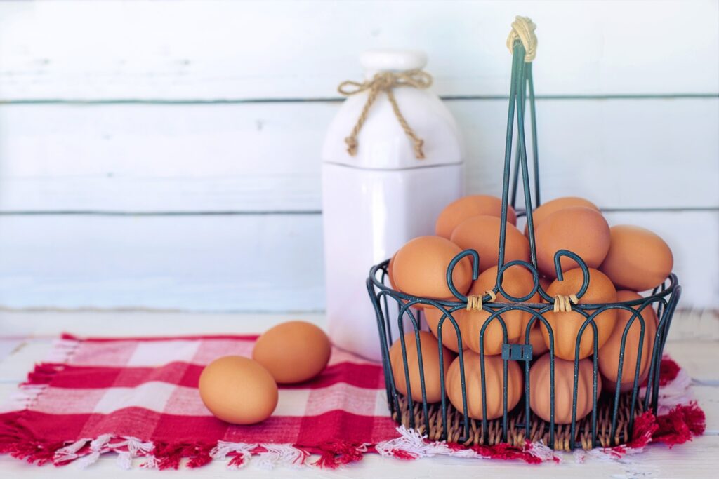 Basket of brown eggs with milk bottle on a Gingham napkin in front of white siding of a home. Collect fresh eggs daily with the Calgary Chicken Rentals program.